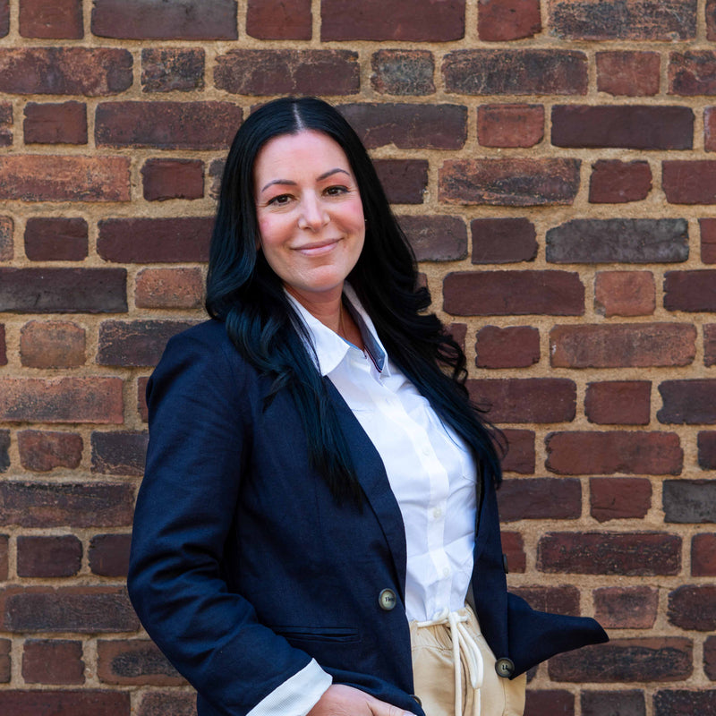 Woman in a navy blazer and white shirt standing against a brick wall